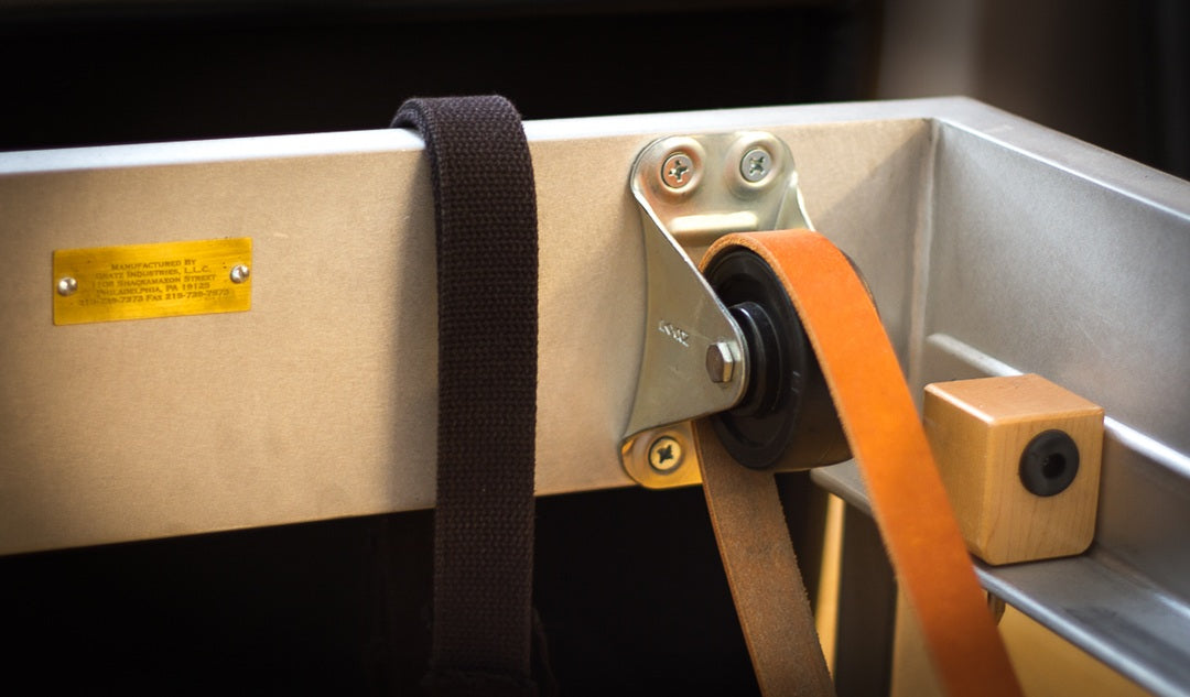 Close-up of a Gratz Pilates reformer pulley with leather and cotton straps threaded through.