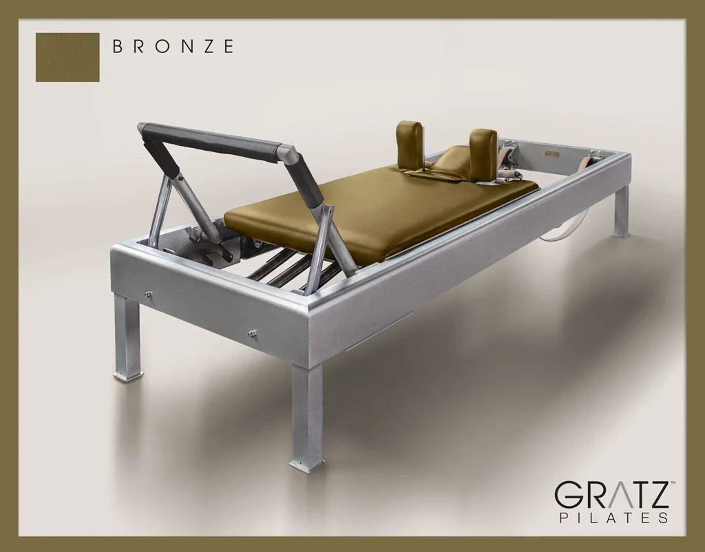 Gratz Pilates Aluminum Archive Reformer Equipment in Bronze color Padded Carriage.  Soft beige background.