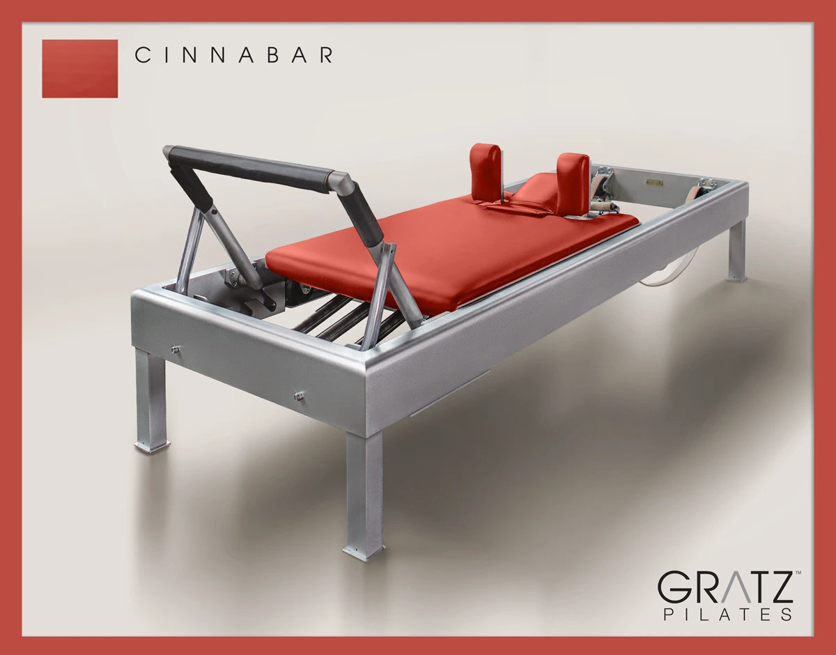 Gratz Pilates Aluminum Archive Reformer Equipment in Cinnabar color Padded Carriage.  Soft beige background.