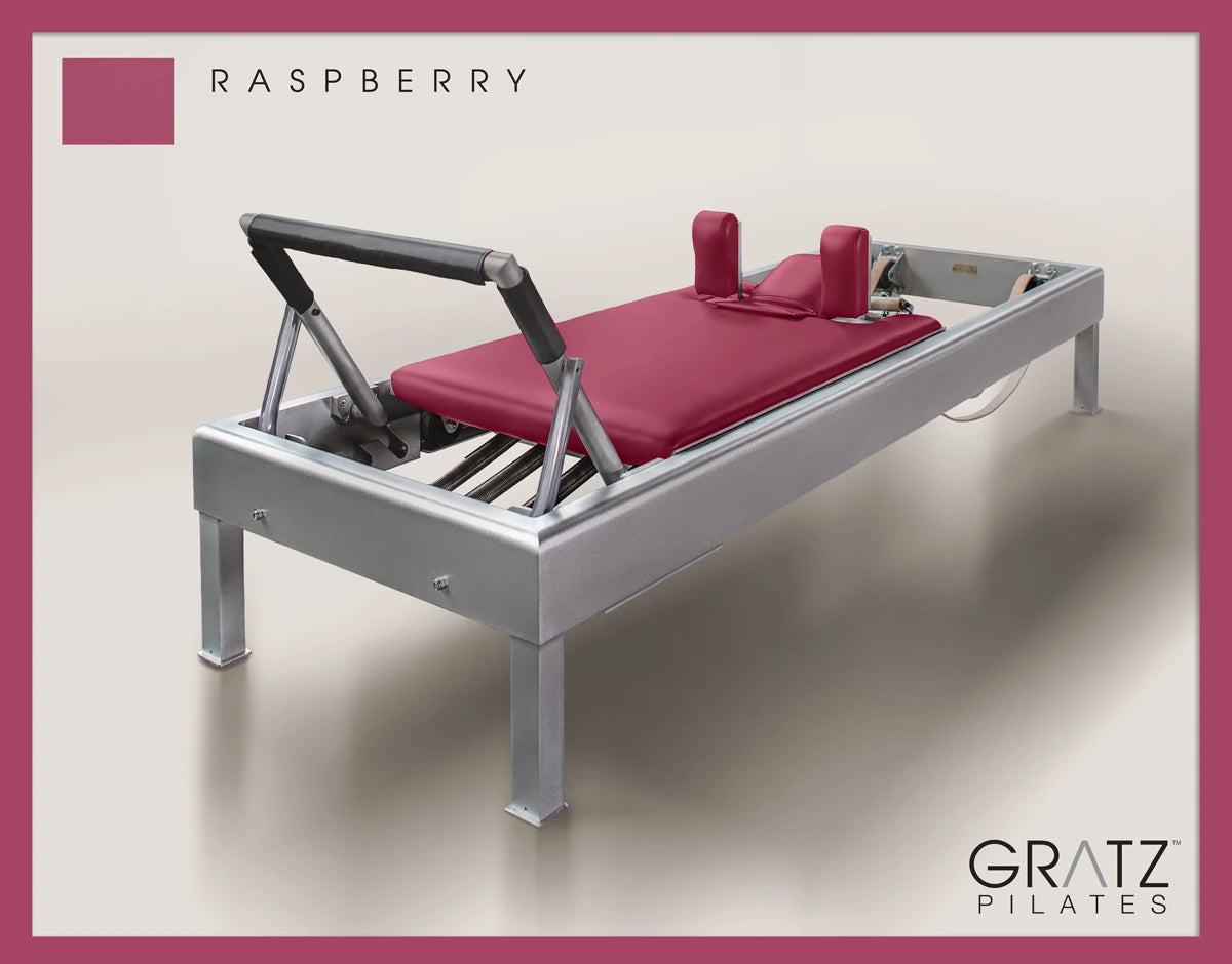 Gratz Pilates Aluminum Archive Reformer Equipment in Raspberry color Padded Carriage. Soft beige background.