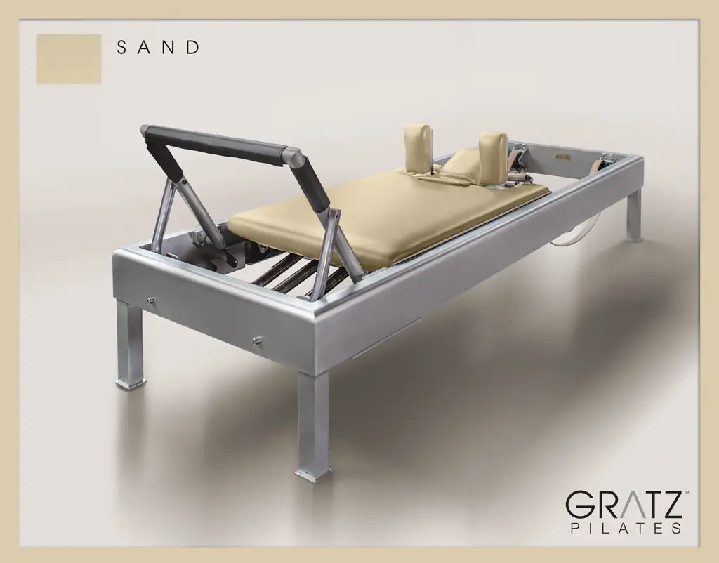 Gratz Pilates Aluminum Archive Reformer Equipment in Sand color Padded Carriage.  Soft beige background.
