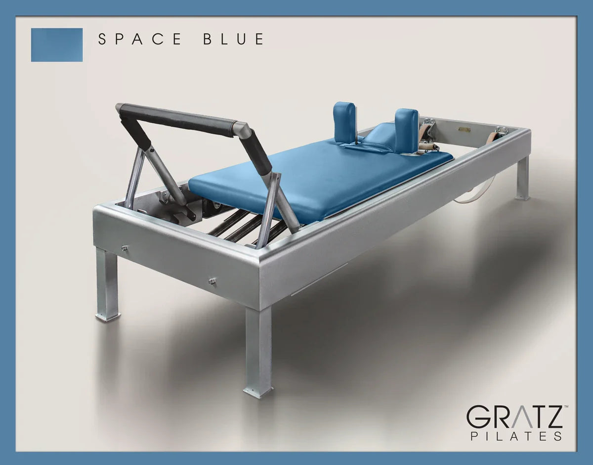 Gratz Pilates Aluminum Archive Reformer Equipment in Space Blue color Padded Carriage. Soft beige background.