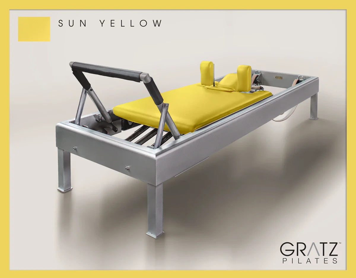 Gratz Pilates Aluminum Archive Reformer Equipment in Sun Yellow color Padded Carriage. Soft beige background.