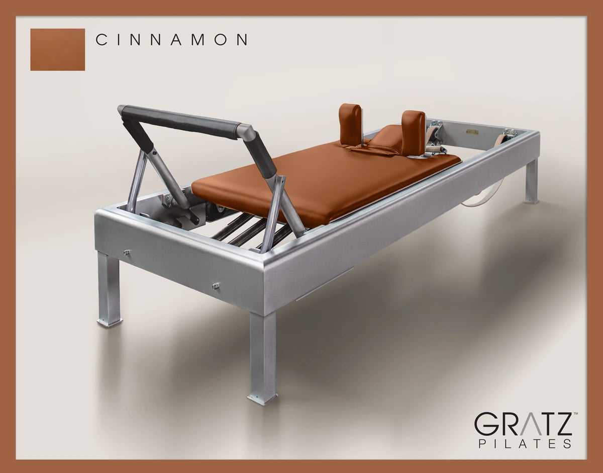 Gratz Pilates Aluminum Archive Reformer Equipment in Cinnamon color Padded Carriage. Soft beige background.
