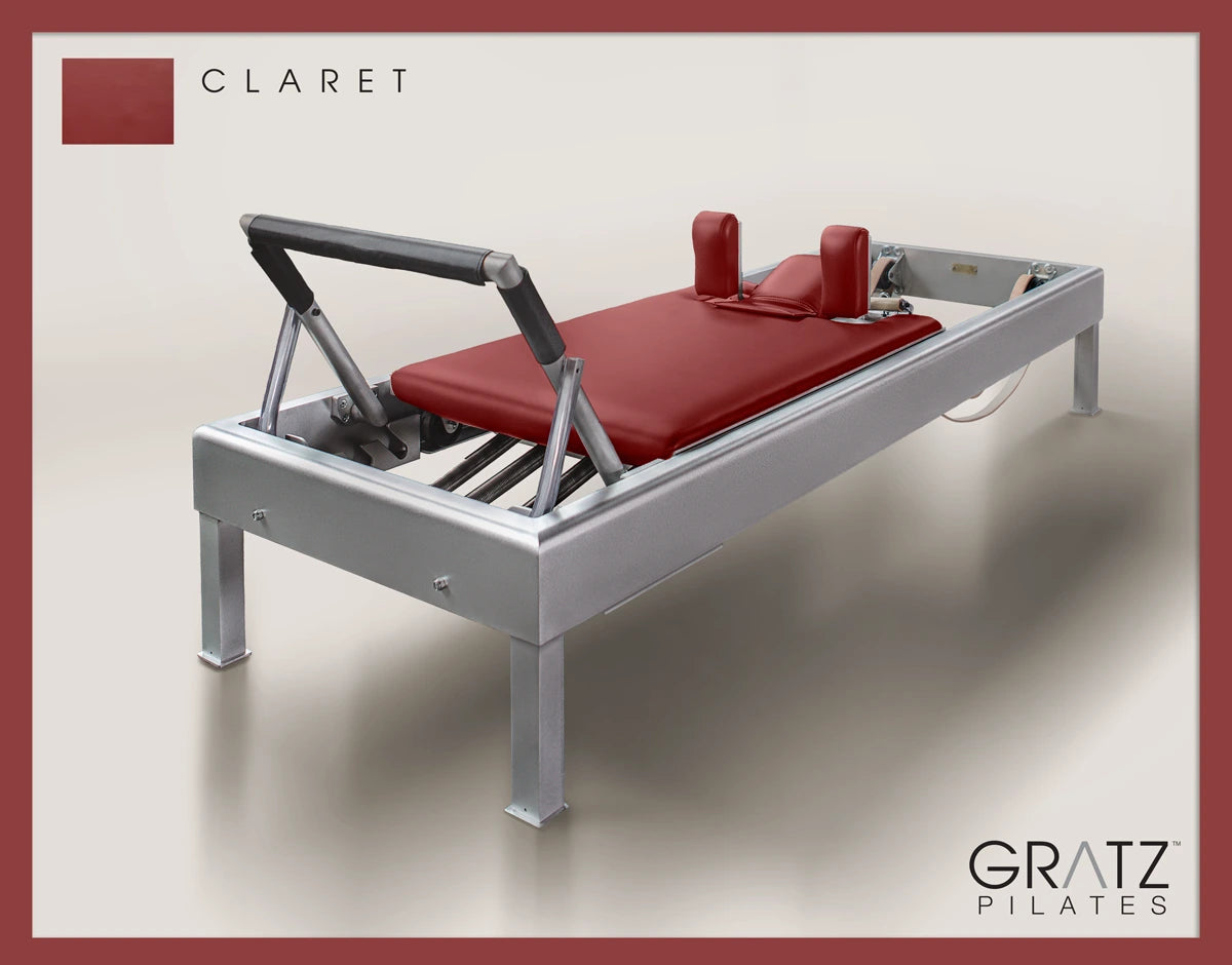 Gratz Pilates Aluminum Archive Reformer Equipment in Claret color Padded Carriage. Soft beige background.