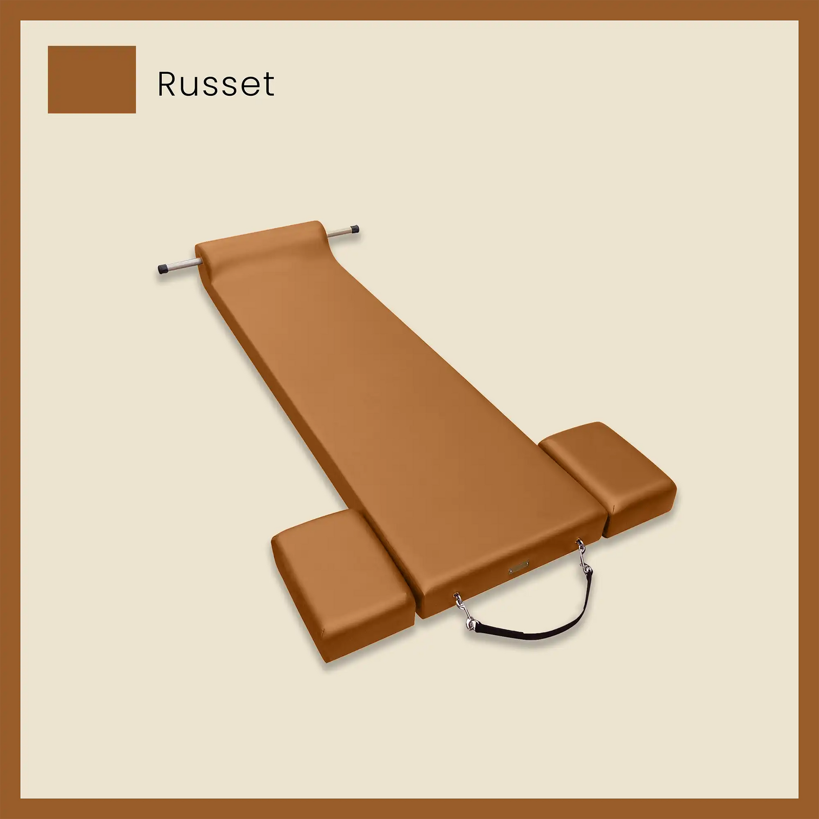 Brown pilates mat with foot strap and side blocks on a neutral beige background.