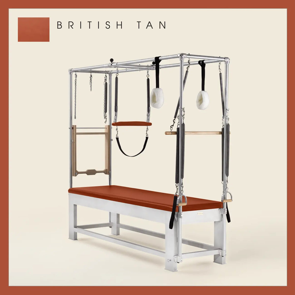 British Tan color Trapeze Table with aluminum frame, adjustable bars, straps, and springs. Premium Pilates equipment against a beige background.