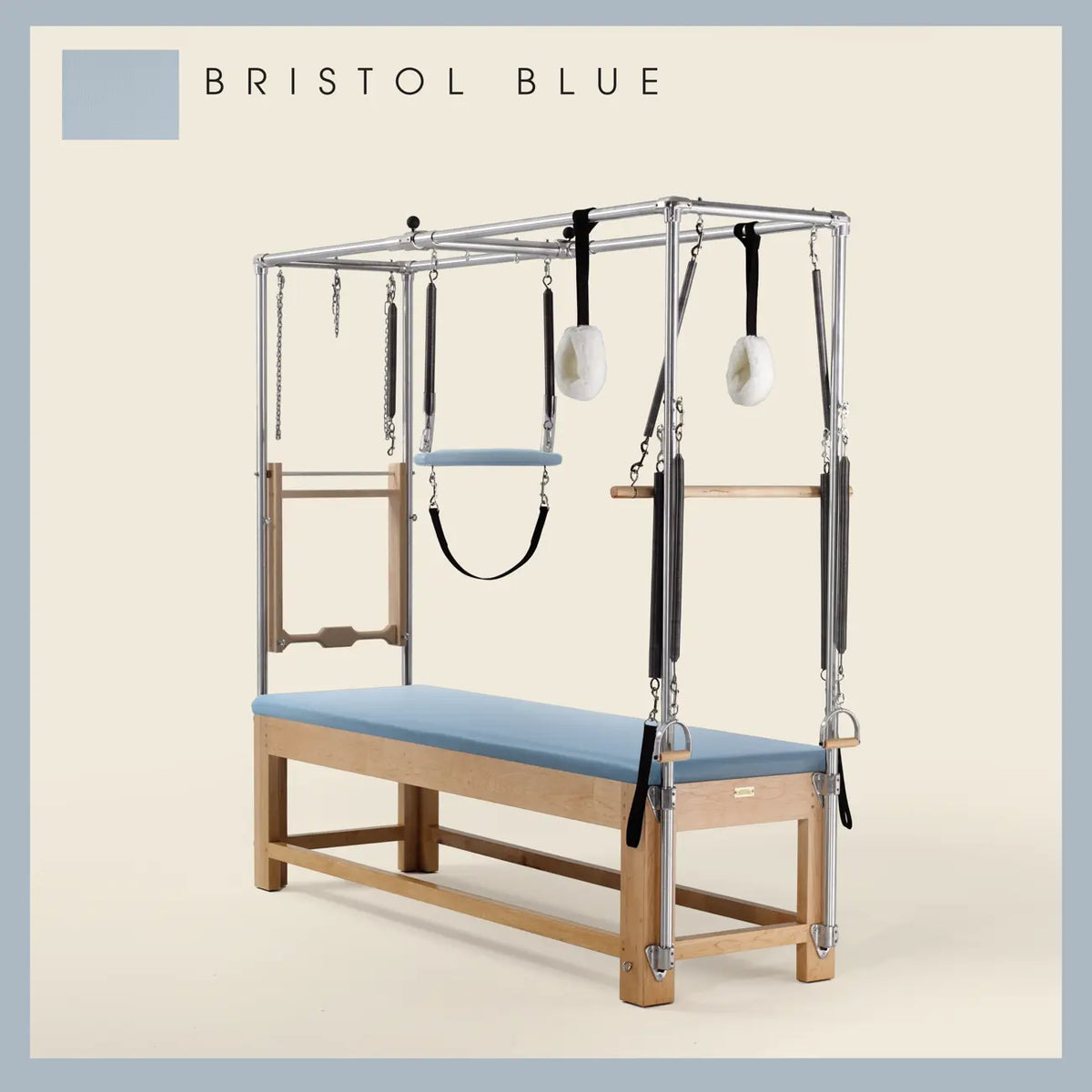 Bristol Blue Pilates Cadillac with maple wood frame, adjustable bars, straps, and springs. Premium Pilates equipment against a beige background.