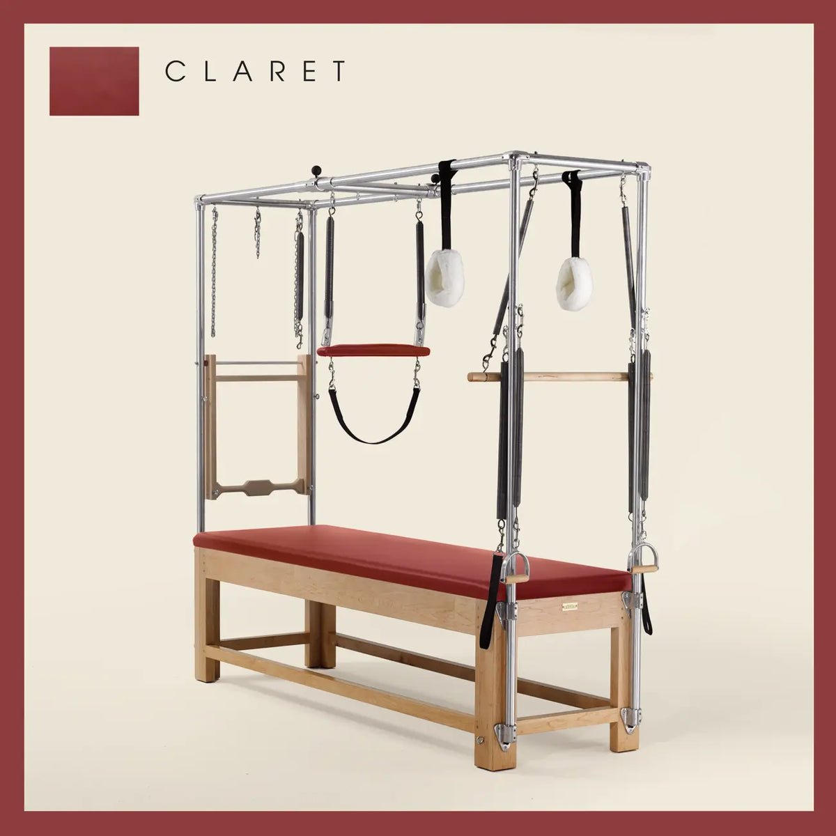Claret color Pilates Cadillac with maple wood frame, adjustable bars, straps, and springs. Premium Pilates equipment against a beige background.