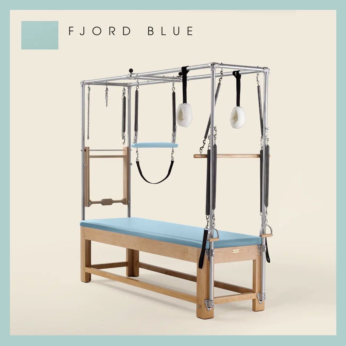 Fjord Blue color Pilates Cadillac with maple wood frame, adjustable bars, straps, and springs. Premium Pilates equipment against a beige background.