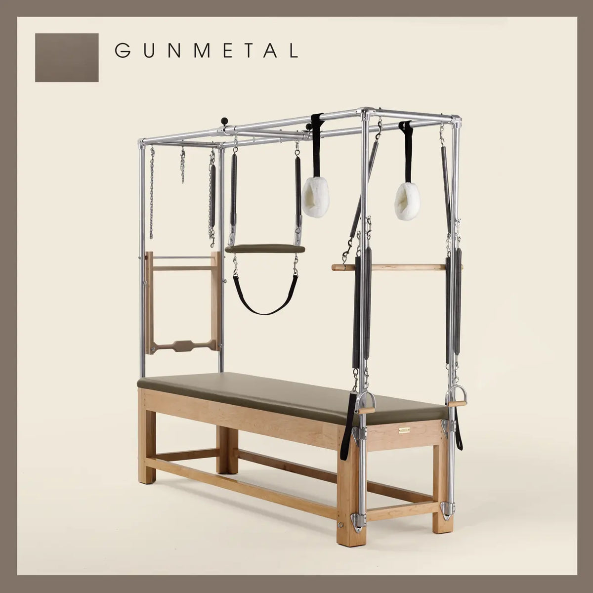 Gunmetal color Pilates Cadillac with maple wood frame, adjustable bars, straps, and springs. Premium Pilates equipment against a beige background.