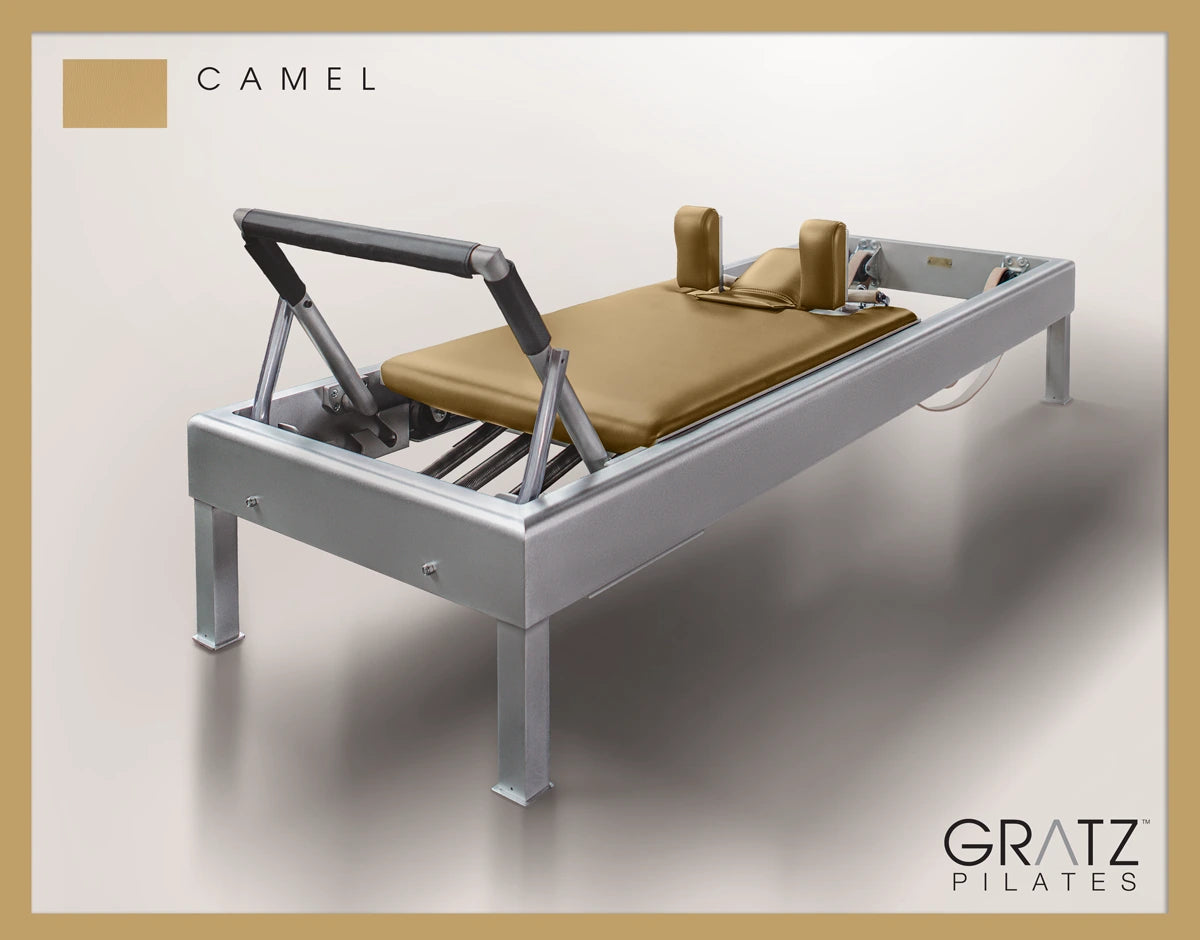 Gratz Pilates Aluminum Archive Reformer Equipment in Camel color Padded Carriage. Soft beige background. 