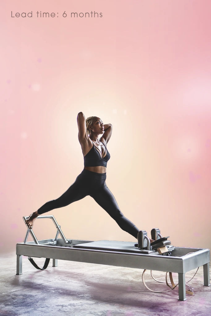 Nicole Smith performs an exercise on a Pilates Reformer in warm pink and yellow lighting. Text reads: "Lead time: 6 months."