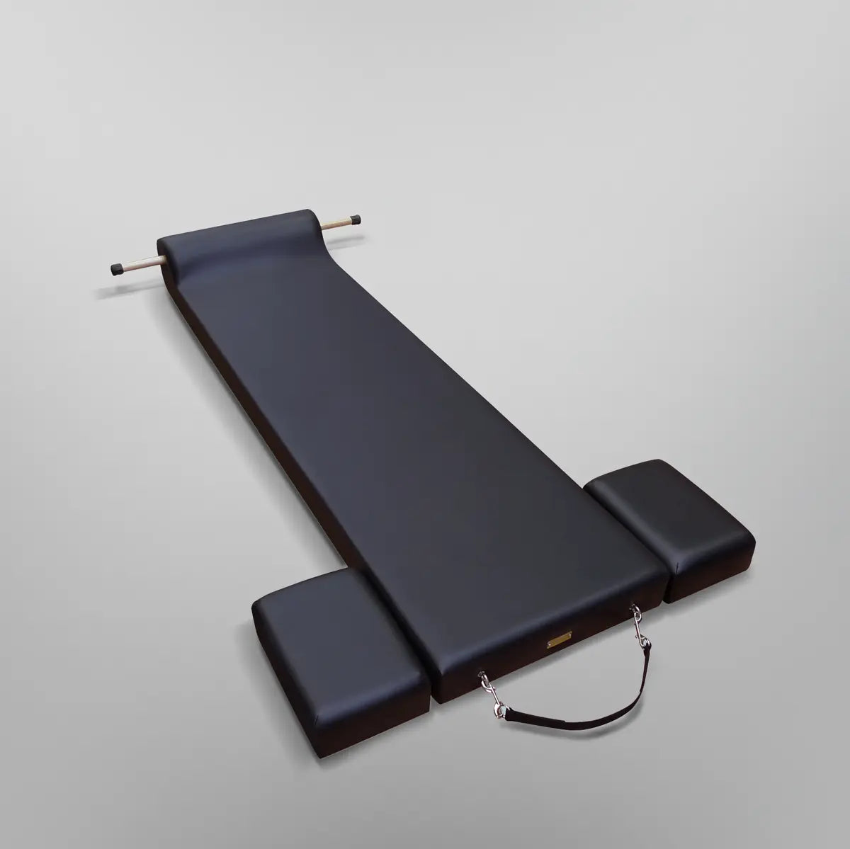 Gratz Pilates contour mat in black with padded headrest, wooden dowel, and carrying strap.