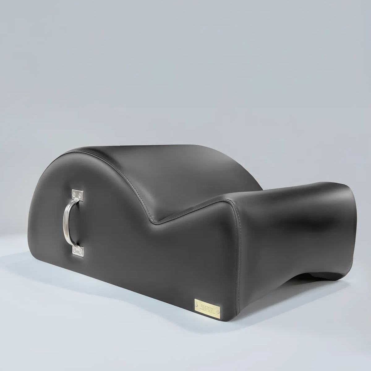 Black upholstered Gratz Pilates spine corrector with a chrome carry handle on a grey backdrop.
