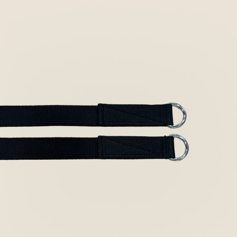 Pilates reformer straps in black canvas with silver D-ring buckles for footwork and strap exercises.